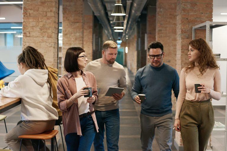 Group of colleagues walking with coffee in hand, showing casual workplace dynamics and coaching hesitation.