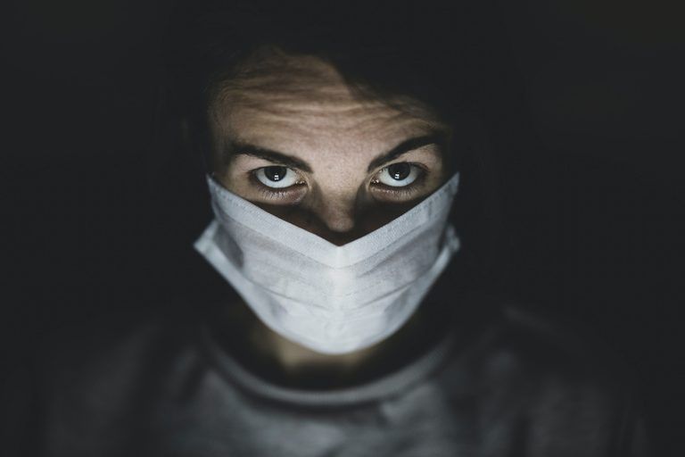 Person wearing a mask in dim lighting, symbolising resilience and steady leadership during uncertain times.