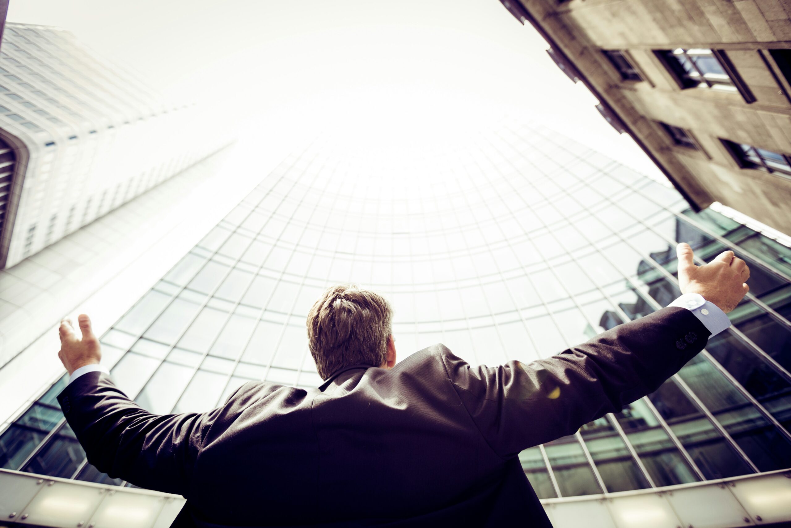 Business leader facing tall buildings with raised arms, reflecting bold leadership in complex sales environments.