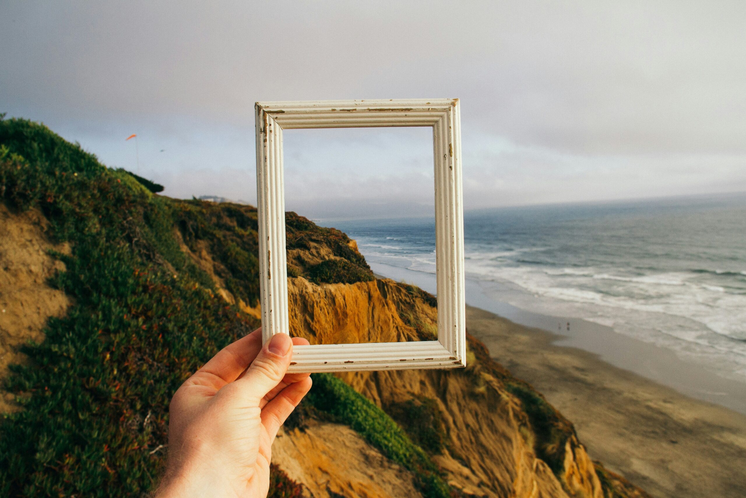 Hand holding an empty picture frame over a scenic landscape, reflecting leadership perspective and coaching clarity.