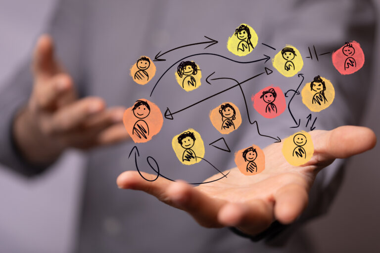 Hand holding a colourful, hand-drawn network of connected people icons, symbolising a collaborative coaching ecosystem and behaviour change across teams.