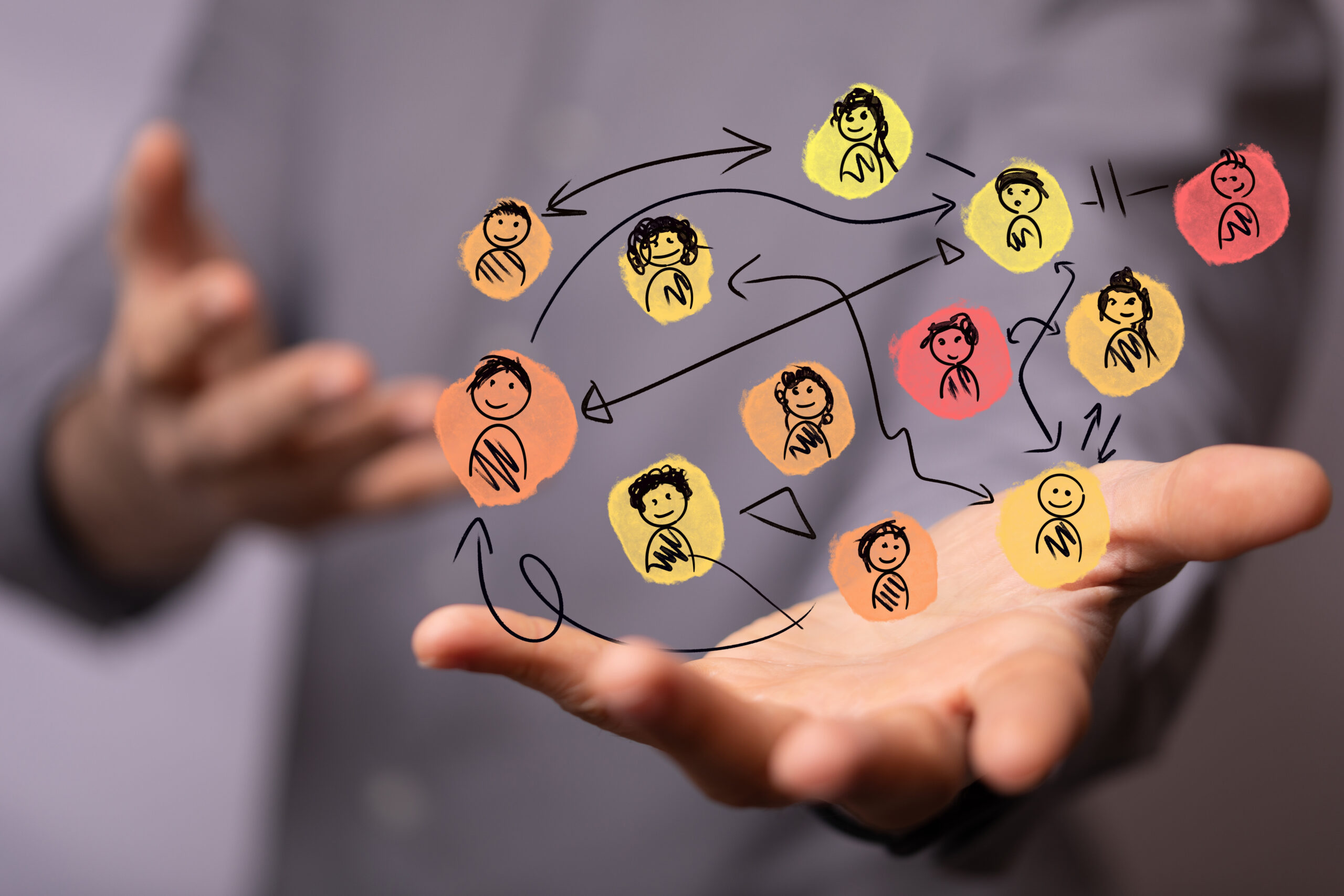 Hand holding a colourful, hand-drawn network of connected people icons, symbolising a collaborative coaching ecosystem and behaviour change across teams.