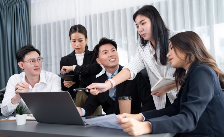 Team of Asian professionals engaged in collaborative discussion, representing a sustained coaching culture built through shared reflection and daily rhythm.
