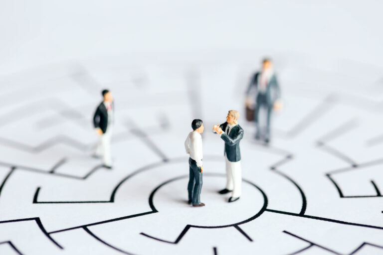 Miniature figures of a manager coaching a salesperson at the centre of a maze, symbolising structured support and rhythm in sales coaching.
