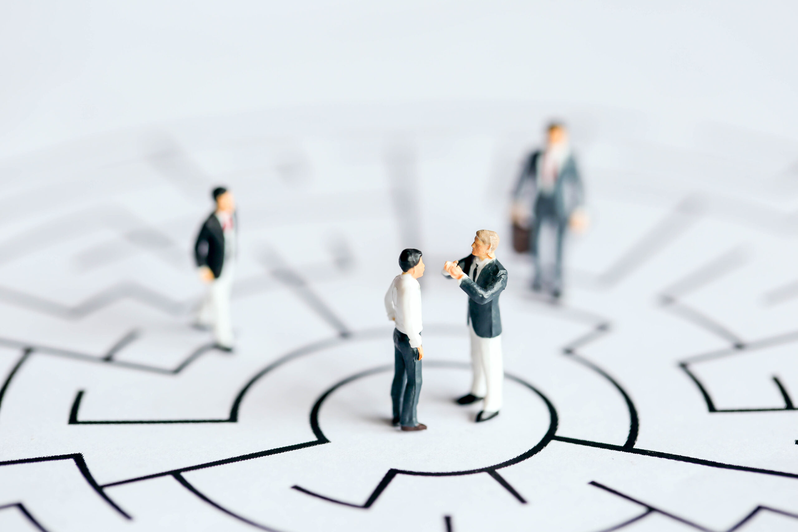 Miniature figures of a manager coaching a salesperson at the centre of a maze, symbolising structured support and rhythm in sales coaching.