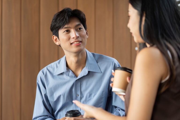 Young Asian man listening attentively during a casual conversation, holding a coffee cup and making eye contact to show genuine interest and curiosity.
